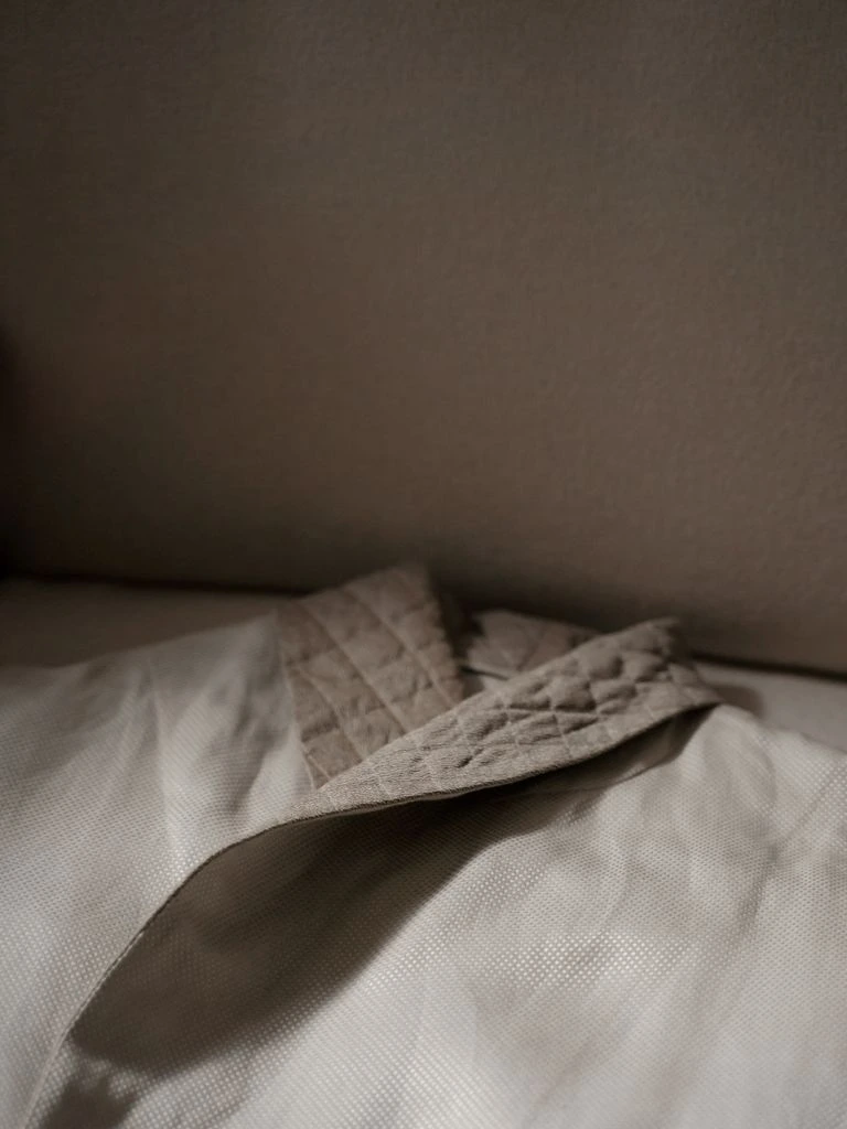 A cream linen overshirt on a wooden hanger in soft daylight