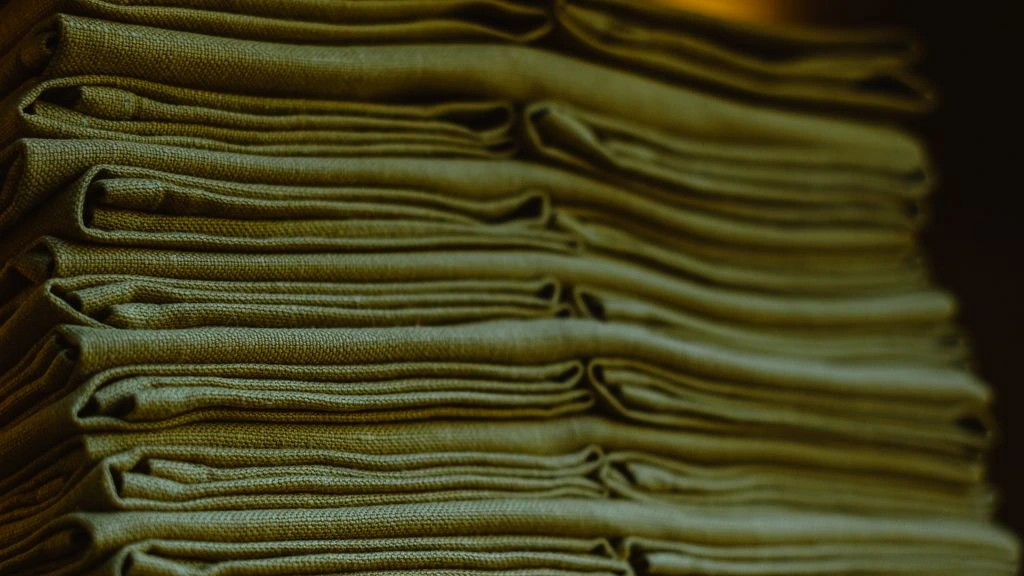 A folded stack of heritage knitwear in cream, oat and rust tones on linen.